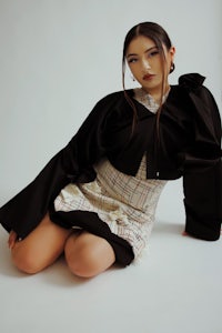 a woman sitting on the floor in a plaid skirt and black jacket